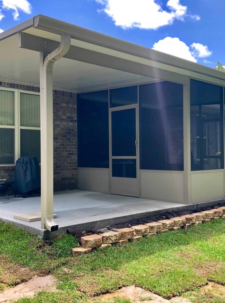 Screened patio enclosure attached to a brick home with a covered roof and concrete floor.